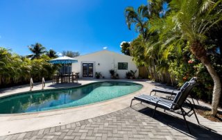Pool deck resurfacing cost considerations for a backyard pool with gray pavers, lounge chairs, and tropical landscaping