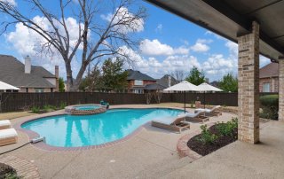 Backyard swimming pool with textured pool deck texture, lounge chairs, umbrellas, and a raised spa.