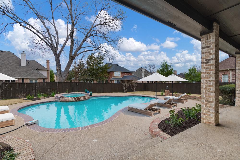 Backyard swimming pool with textured pool deck texture, lounge chairs, umbrellas, and a raised spa.