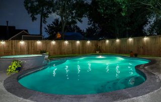 Backyard swimming pool with turquoise water, dark pool deck colors, and outdoor lighting creating a relaxing nighttime atmosphere.