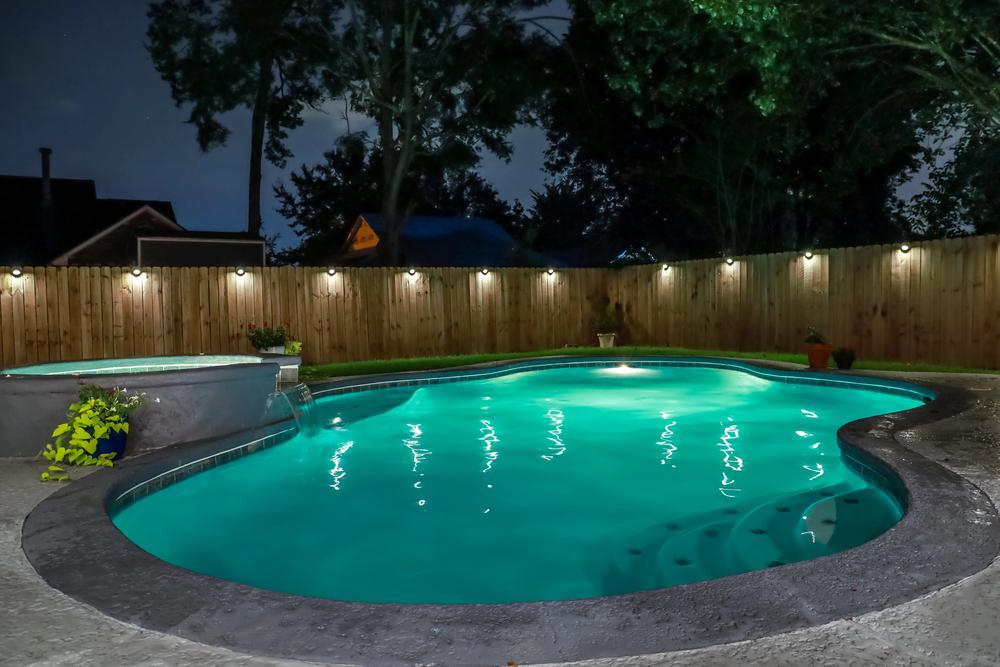 Backyard swimming pool with turquoise water, dark pool deck colors, and outdoor lighting creating a relaxing nighttime atmosphere.