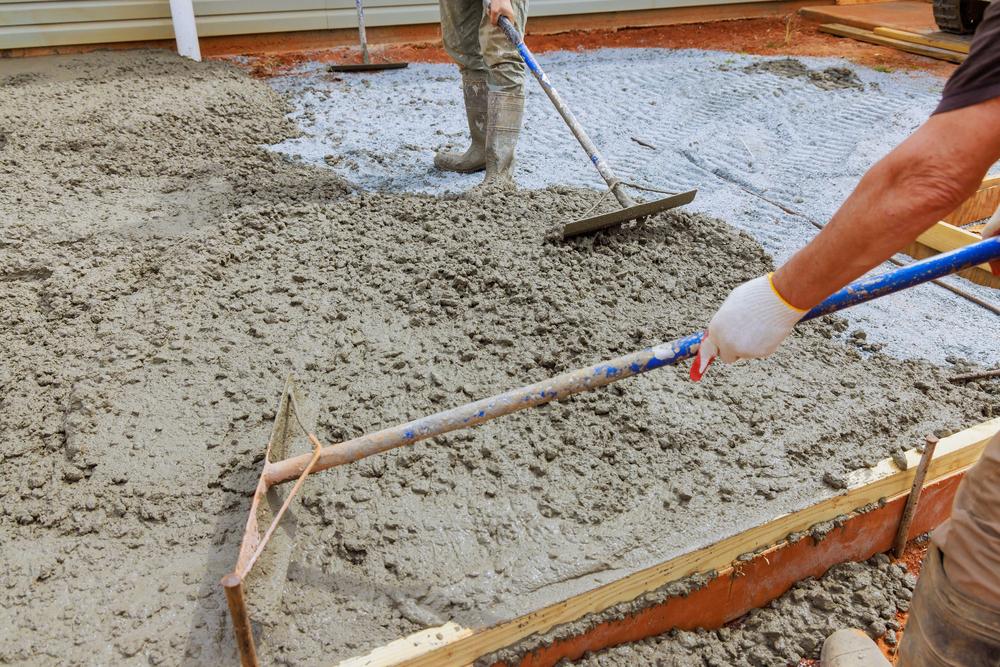 Concrete resurfacing contractor leveling and spreading freshly poured concrete using professional tools for a smooth, even surface.